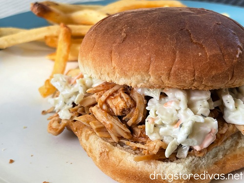 A pulled chicken barbecue sandwich with coleslaw on a plate with fries in the back.