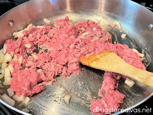 Raw ground turkey and diced onions being stirred with a bamboo spoon in a silver pan.