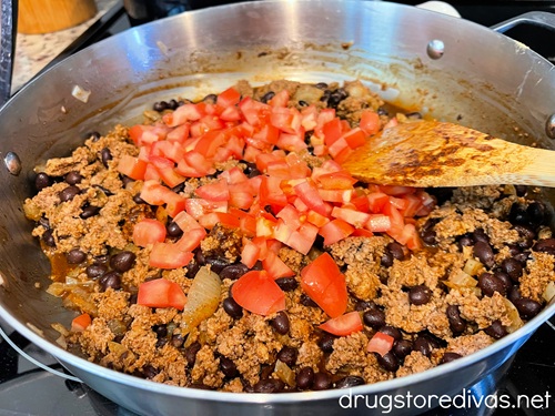 Diced tomatoes on top of a ground turkey and black beans mixture in a silver pan with a bamboo spoon in the pan.