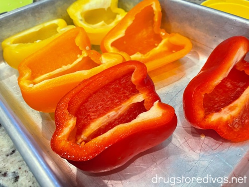 A yellow, orange, and red pepper cut in half on a silver tray.
