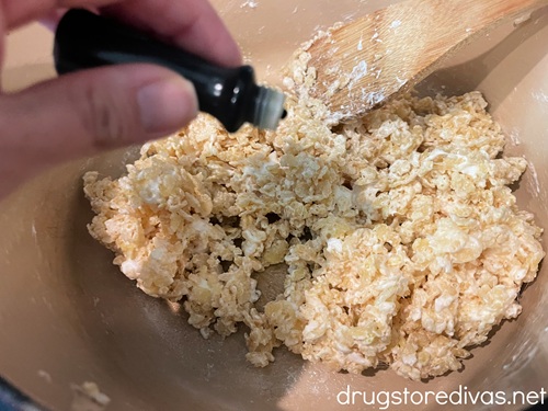 A hand adding green food coloring to a marshmallow and rice cereal mixture.