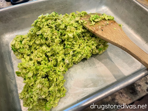 Green rice krispies treats in a silver cake pan with a bamboo spoon next to it.