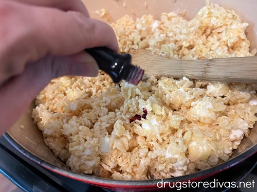 A hand adding red food coloring to a marshmallow and rice cereal mixture.