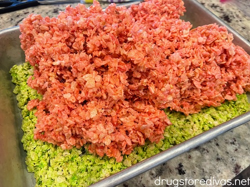 Pink rice krispies treats on top a light green layer of rice krispies treats in a silver cake pan.