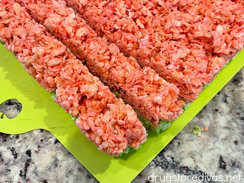 Cut strips of pink and green layered rice krispies treats on top of a green cutting board.