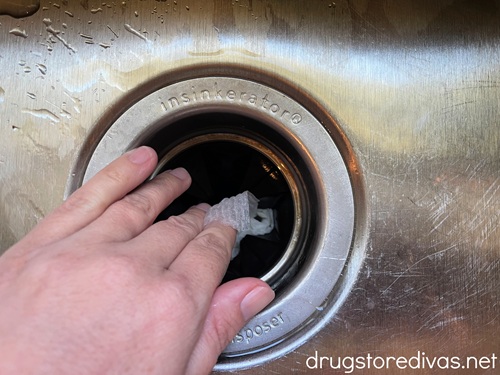A hand holding a paper towel and washing the splash guard of a garbage disposal.