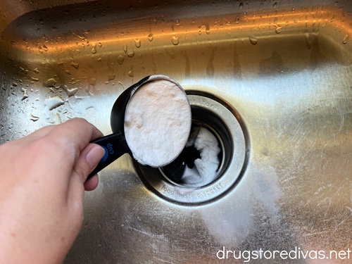 Baking soda in a measuring cup being poured down a garbage disposal.