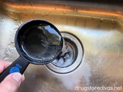 A clear liquid in a measuring cup being poured down a garbage disposal.