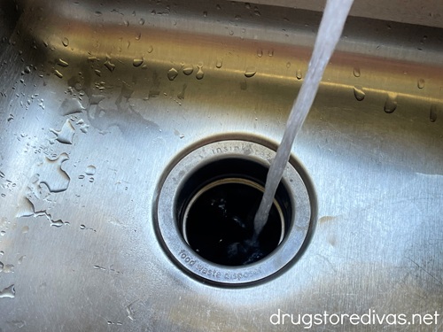 Water being poured from a tap down a garbage disposal in a sink.