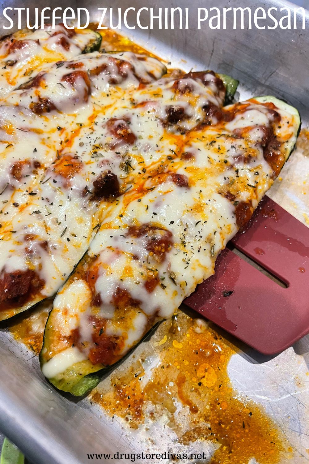 Three stuffed zucchinis with melted cheese on top in a silver pan, with one being picked up with a red spatula, and the words 