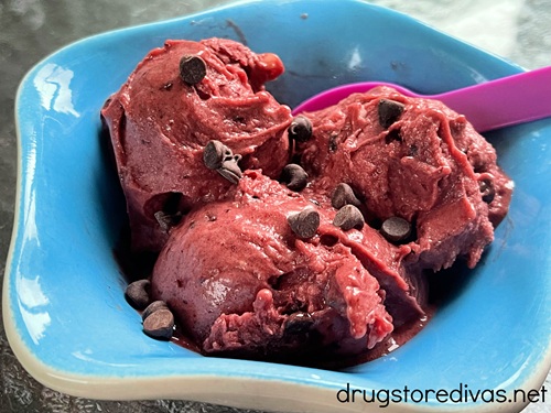 Three scoops of chocolate cherry ice cream in a blue bowl with a purple spoon in it.