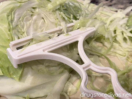 Shredded cabbage with a white cabbage peeler on top.