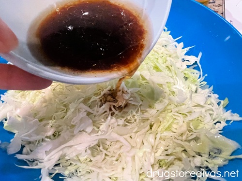 A small bowl with a brown liquid in it being poured over shredded cabbage in a blue bowl.