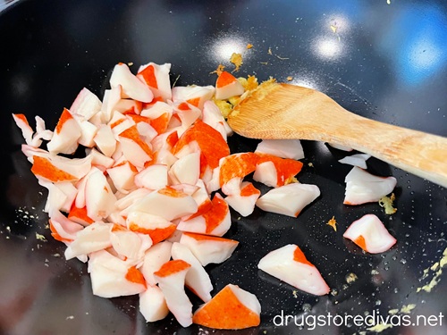 Imitation crab pieces and a bamboo spoon in a wok.