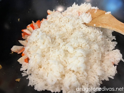Imitation crab pieces, white rice, and a bamboo spoon in a wok.