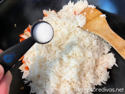 A measuring spoon above imitation crab pieces, white rice, and a bamboo spoon in a wok.