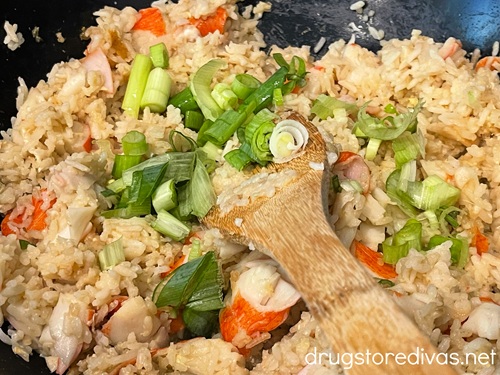 Crab fried rice, with green onion, in a wok with a bamboo spoon.