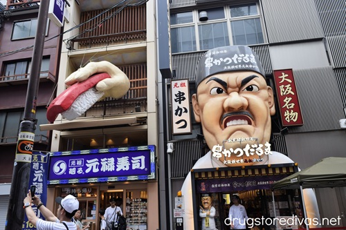 A large angry sushi cook facade and a hand holding a piece of sushi above the Kushikatsu Daruma restaurant in Dotonbori Japan.