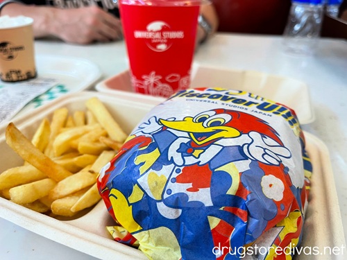 A burger wrapped in Woody Woodpecker paper next to fries and a drink in a red cup from Mel's Drive-In in Universal Studios Japan.