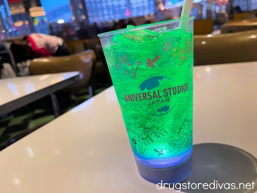 A light-up cup from Universal Studios Japan with a green drink and a white straw in it on a table.