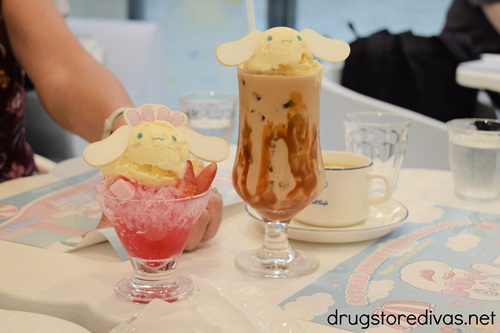 A red sno cone drink and an iced coffee, with a coffee cup behind it, on a table at Cinnamoroll Cafe in Osaka.