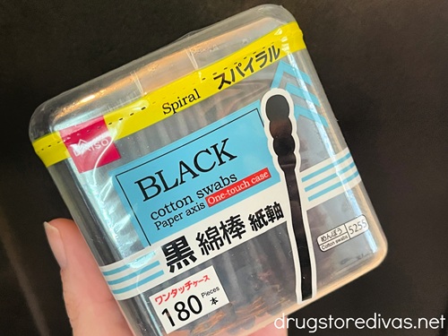 A hand holding a package of black cotton swabs.