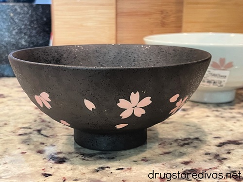 A black bowl with cherry blossoms on it with a white bowl with cherry blossoms in the background.
