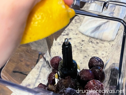A hand squeezing a lemon above a blender filled with cherries.