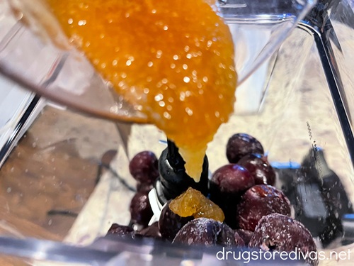Honey in a measuring cup being poured on top of cherries in a blender.