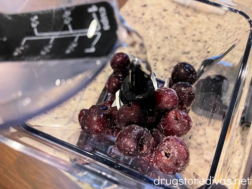 Water in a measuring cup being poured on top of cherries in a blender.