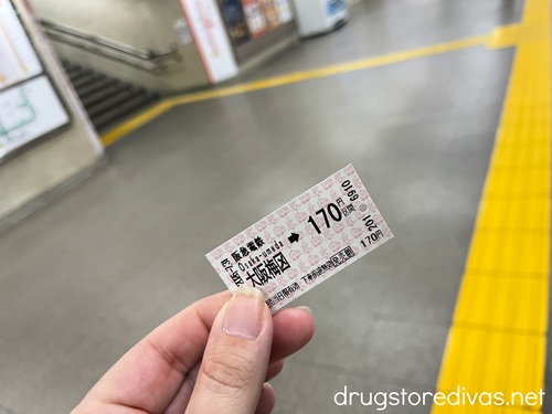 Fingers holding a Japan Railways train ticket in a train station.