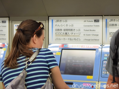 A woman in a blue striped shirt buying a train ticket at a station in Japan.