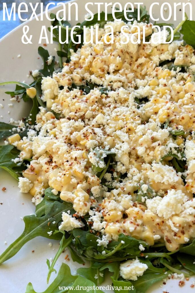 Corn and white crumbled cheese on top of arugula with the words "Mexican Street Corn & Arugula Salad" digitally written on top.