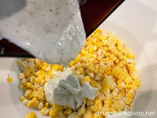 Dressing being poured from a bowl onto corn kernels in a bowl.