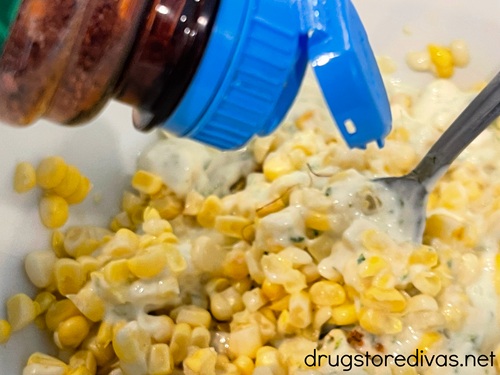 A bottle of Tajin seasoning being poured on top of corn kernels in a bowl.