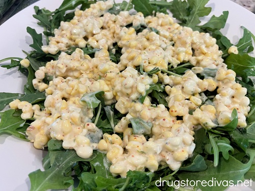 Corn kernels in a white dressing on top arugula.