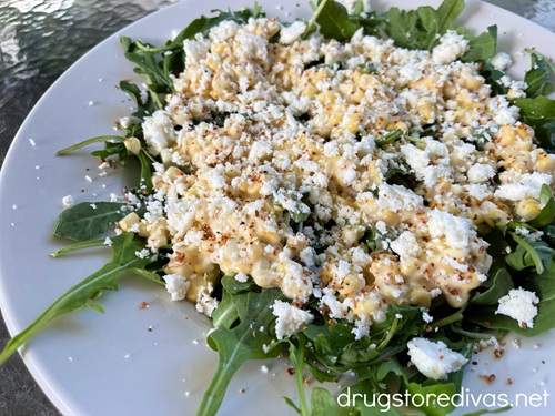 Mexican street corn and arugula salad in a white bowl.
