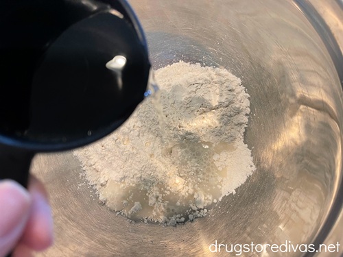 A hand holding a measuring cup of water above a silver bowl.