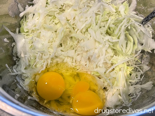 Shredded cabbage and two cracked eggs in a silver bowl.