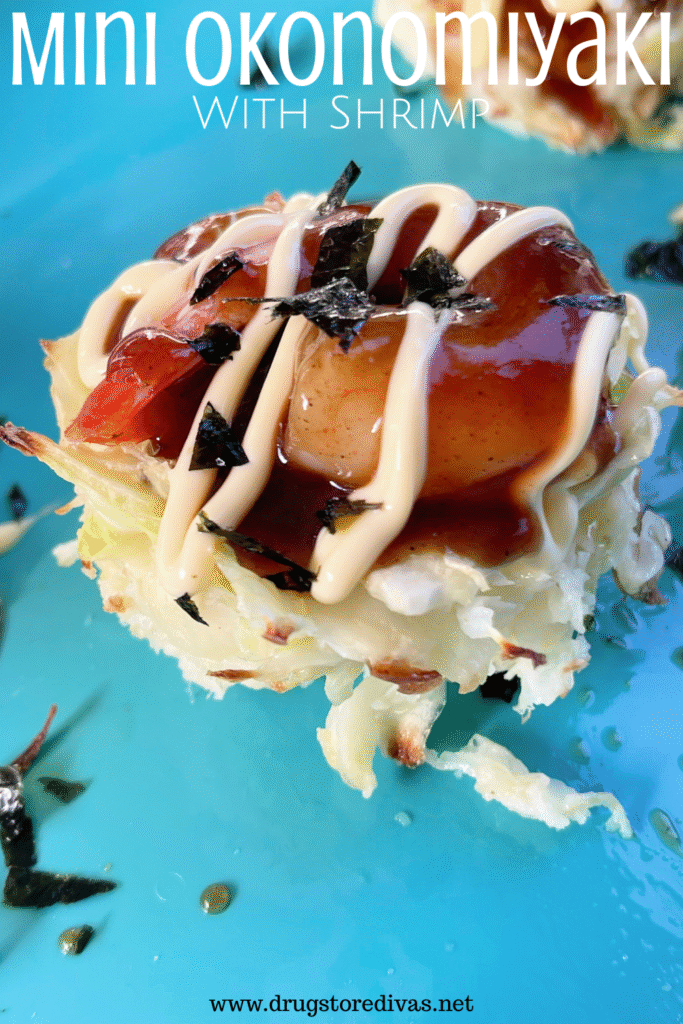 A cabbage pancake with a shrimp, dark sauce, and mayo drizzle on top on a blue tray with the words "Mini Okonomiyaki With Shrimp" digitally written on top.