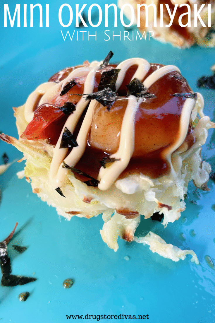 A cabbage pancake with a shrimp, dark sauce, and mayo drizzle on top on a blue tray with the words 
