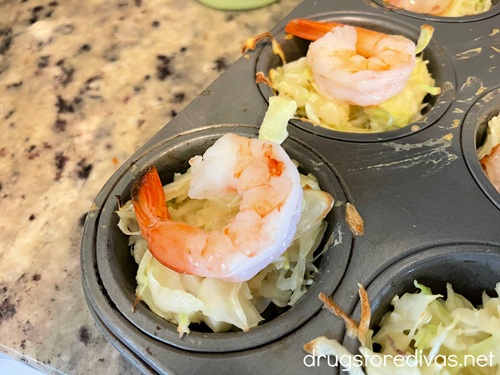 Jumbo shrimp on top of shredded cabbage in cavities in a muffin pan.
