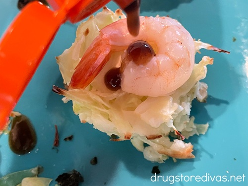 Mini okonomiyaki with shrimp on a blue tray being drizzled with a dark syrup.