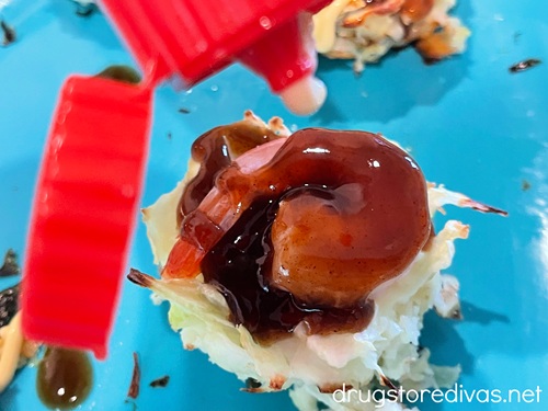 Mini okonomiyaki with shrimp with a dark syrup on them on a blue tray being drizzled with mayo.