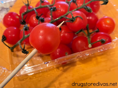 A cherry tomato on a skewer above a box of cherry tomatoes.
