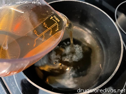 A light brown liquid in a measuring cup being poured into a stock pot.