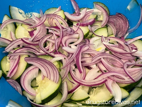 Red onion slices and cucumber pieces in a blue bowl.