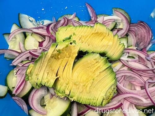 Sliced avocado, red onion slices, and cucumber pieces in a blue bowl.