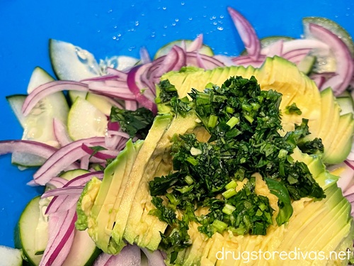 Chopped cilantro, sliced avocado, red onion slices, and cucumber pieces in a blue bowl.
