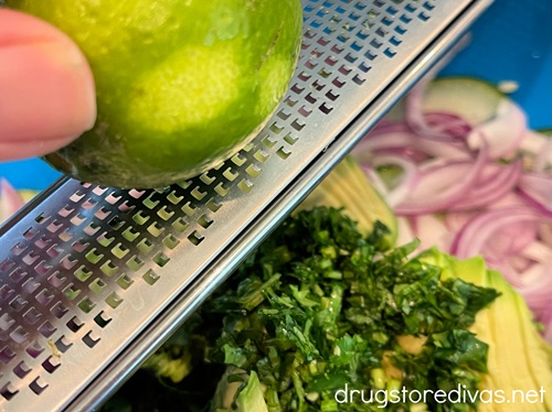 A lime being zested on a microplane grater into a salad.